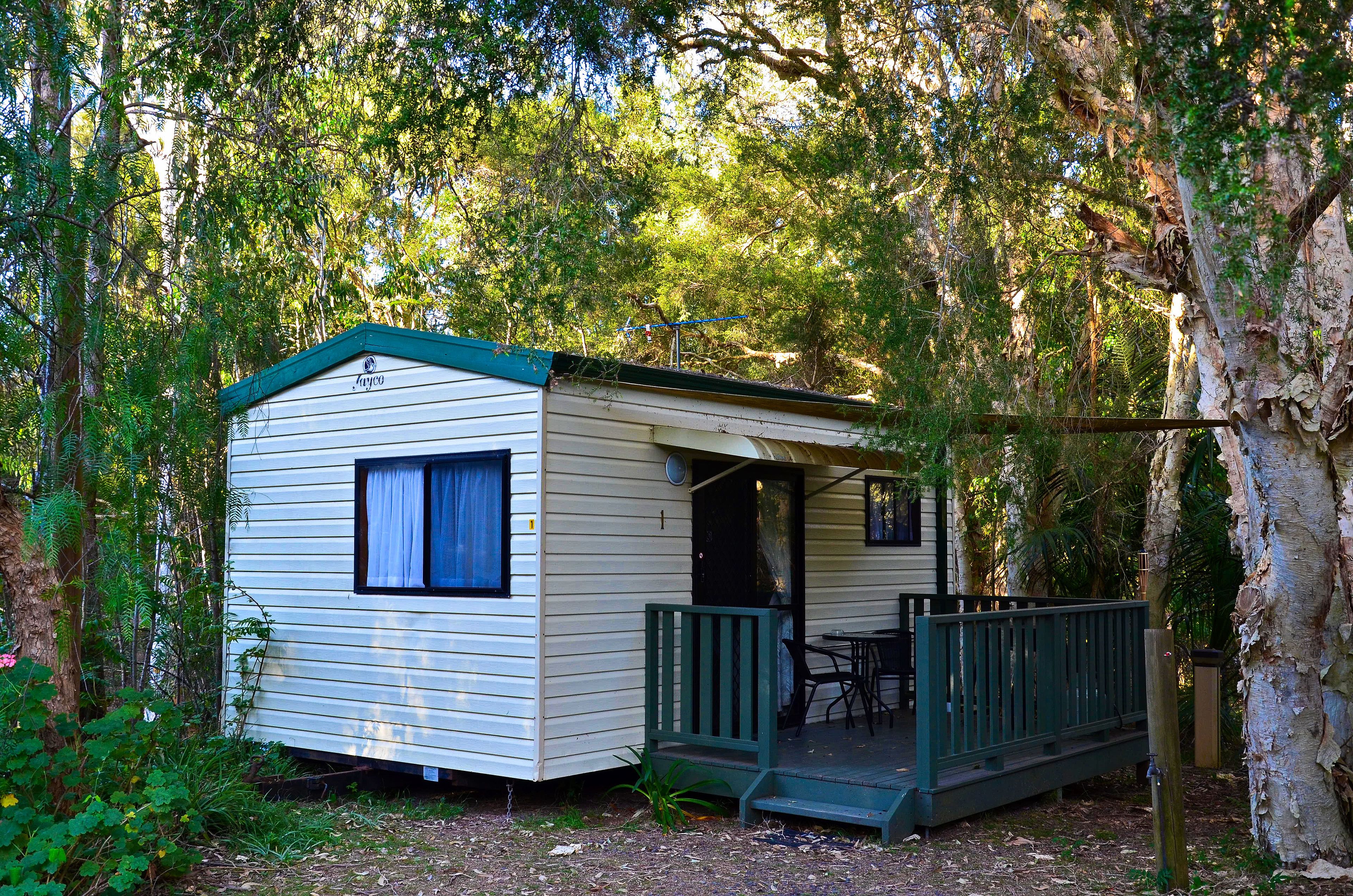 A small, single-story mobile home with a porch and a table and chairs outside.