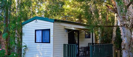 A small, single-story mobile home with a porch and a table and chairs outside.