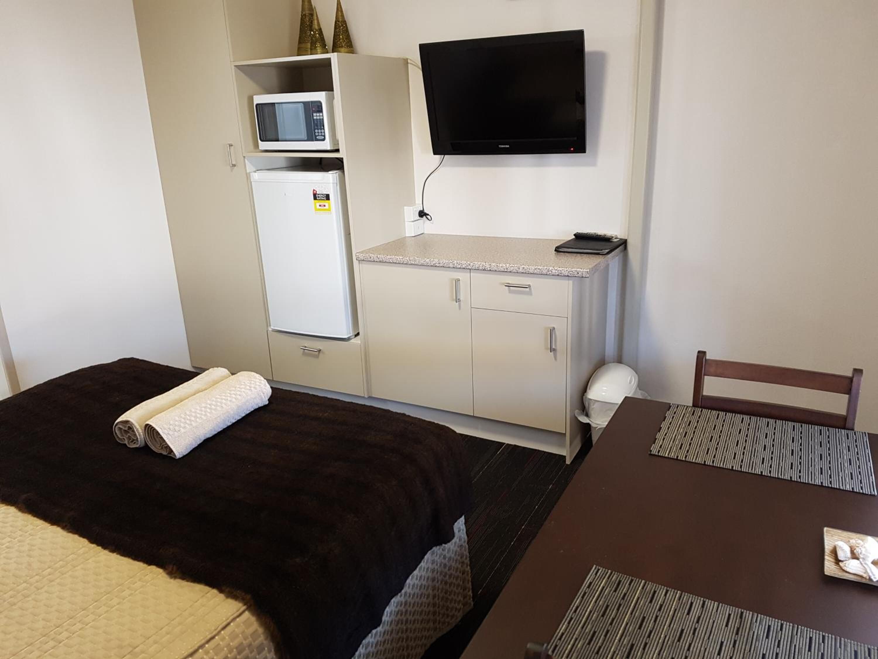 A compact hotel room with a bed, a desk, a television, a microwave, and a refrigerator.