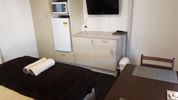 Ein kompaktes Hotelzimmer mit Bett, Schreibtisch, Fernseher, Mikrowelle und Kühlschrank.