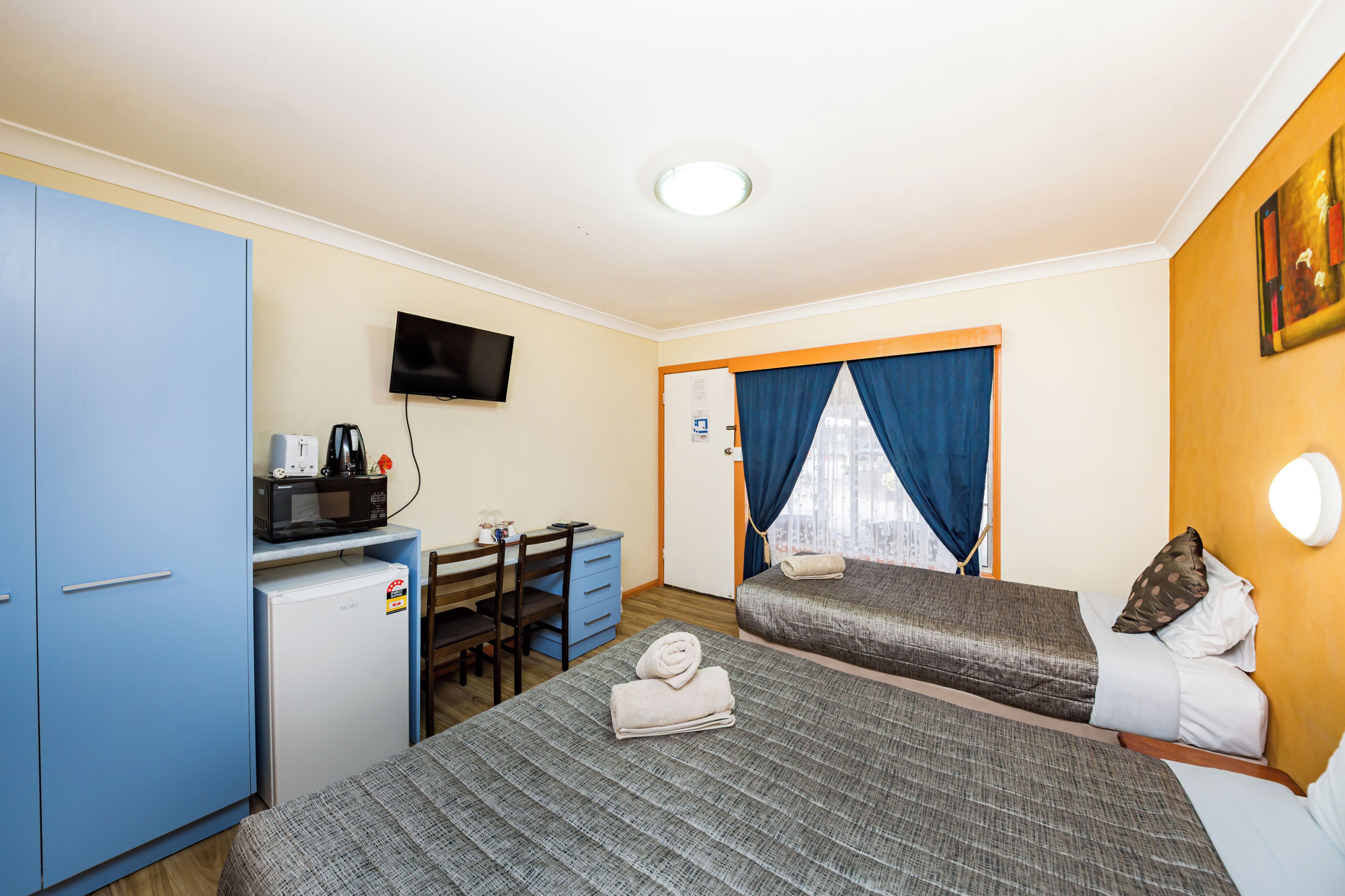 A hotel room with two beds, a desk, a television, and a small refrigerator.