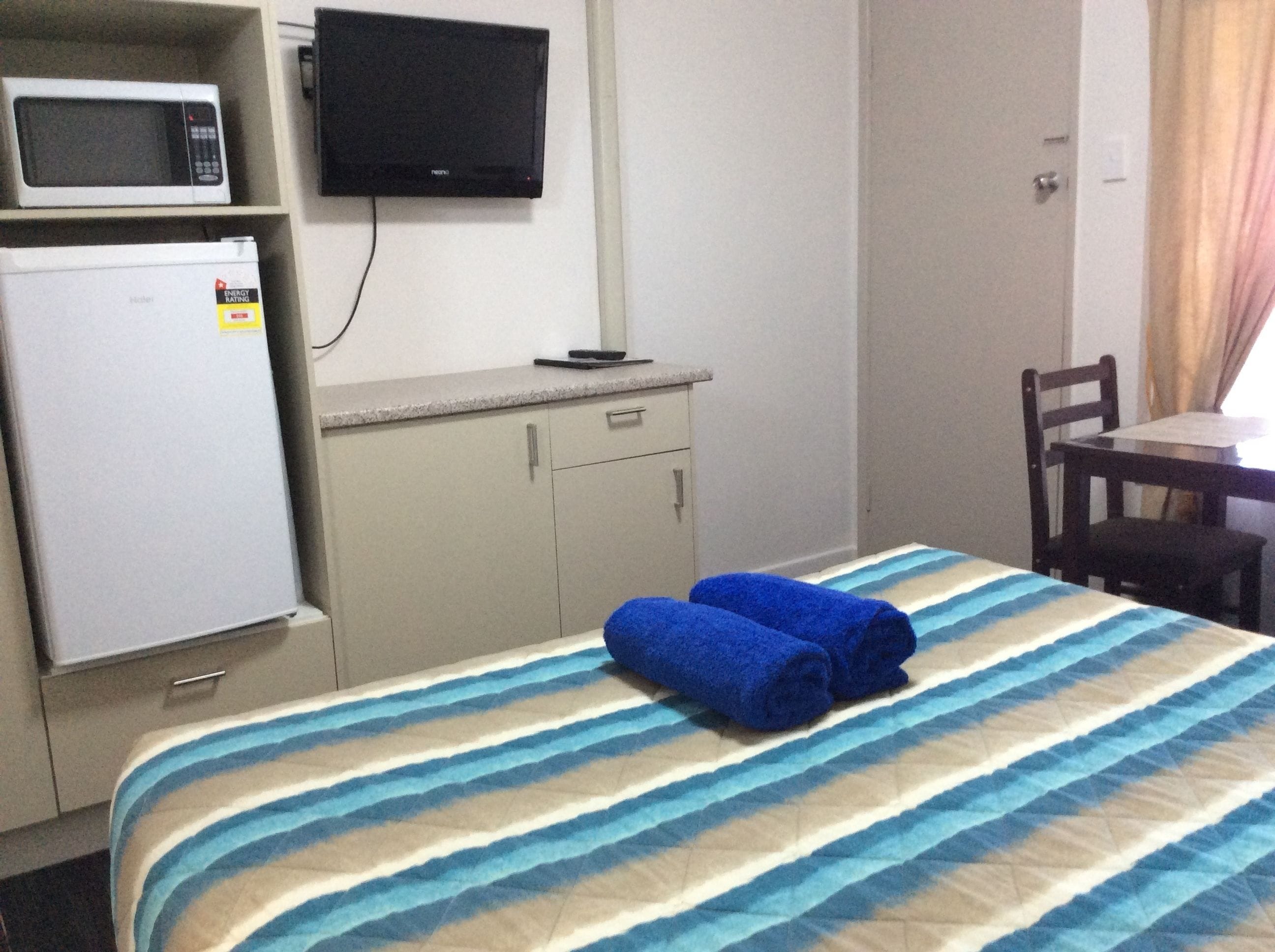 Een hotelkamer met een bed, een magnetron, een koelkast, een televisie en een bureau met stoel.