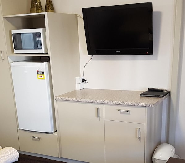A kitchenette with a microwave, refrigerator, and a flat-screen TV mounted on the wall. - Kingaroy Country Motel (Kingaroy)