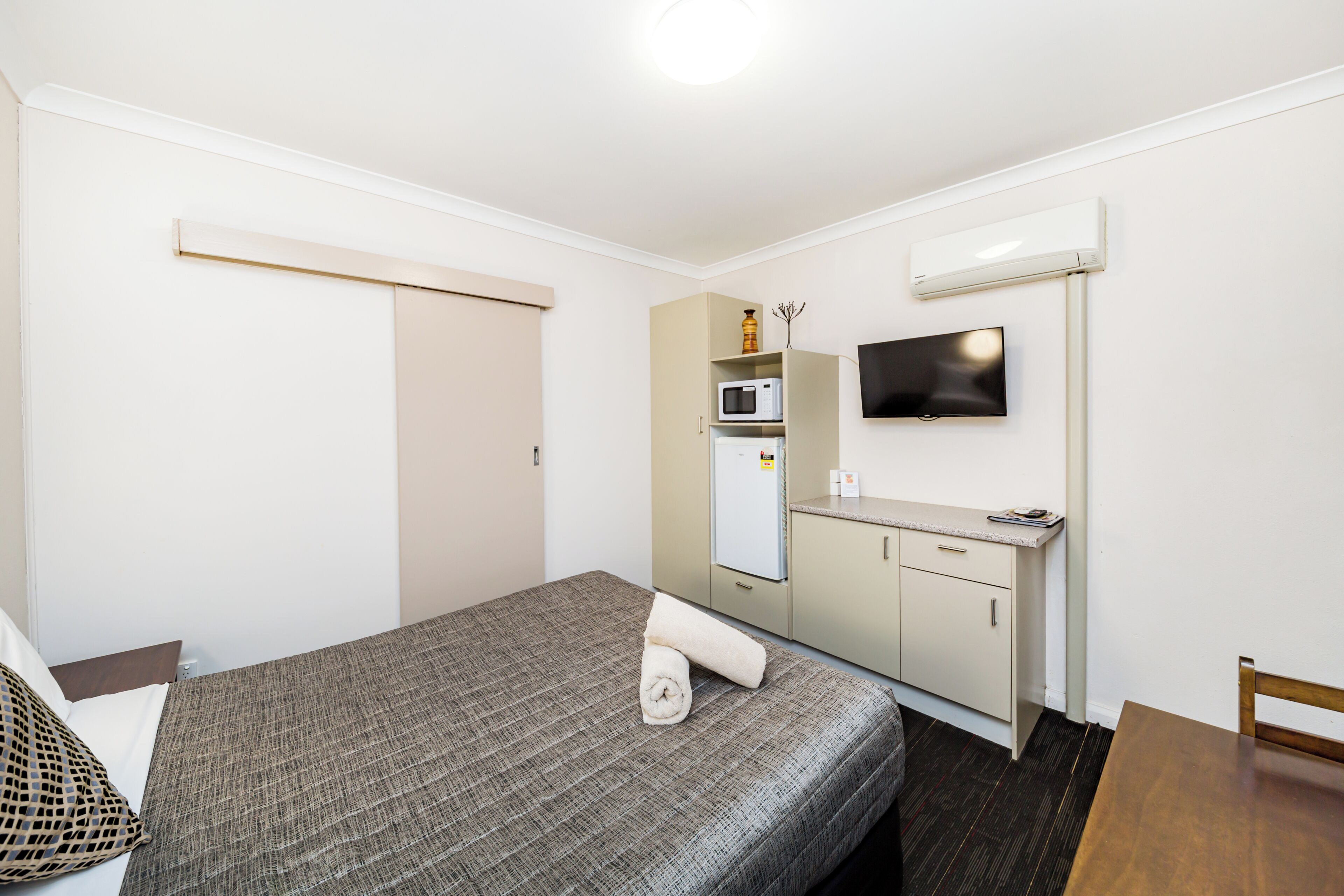 A compact room with a bed, a small kitchenette, a TV, and a wooden table.