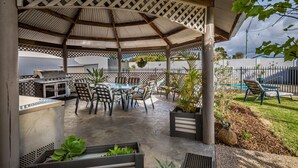 A covered patio with a grill, dining table, chairs, and planters. - Kingaroy Country Motel (Kingaroy)