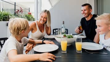 A family dining at an outdoor table with a view of a garden and a fence.