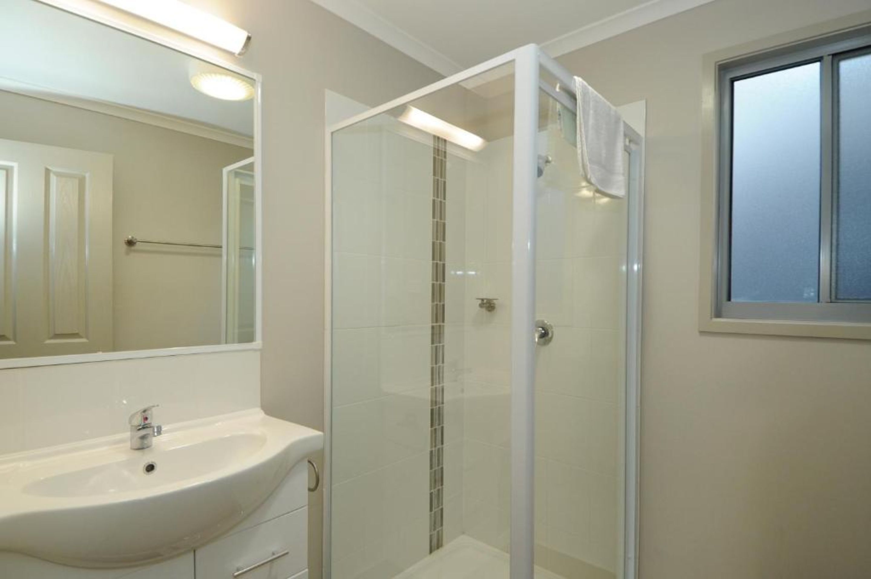 A bathroom with a glass-enclosed shower, a sink, and a large mirror.