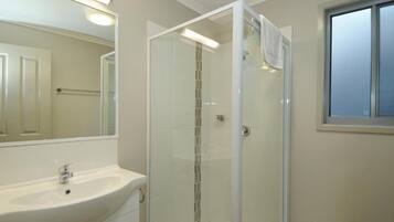 A bathroom with a glass-enclosed shower, a sink, and a large mirror.