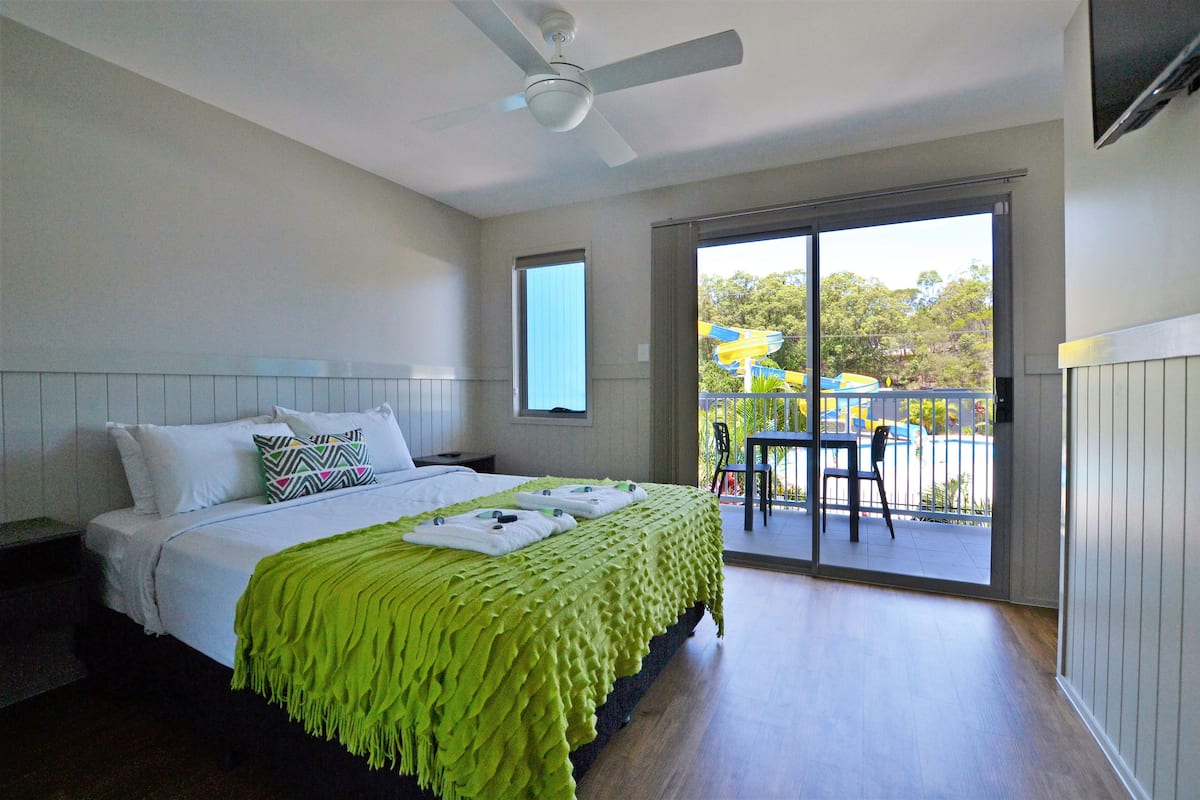 A bedroom with a bed, a ceiling fan, a window, and a view of an outdoor area with a table and chairs.