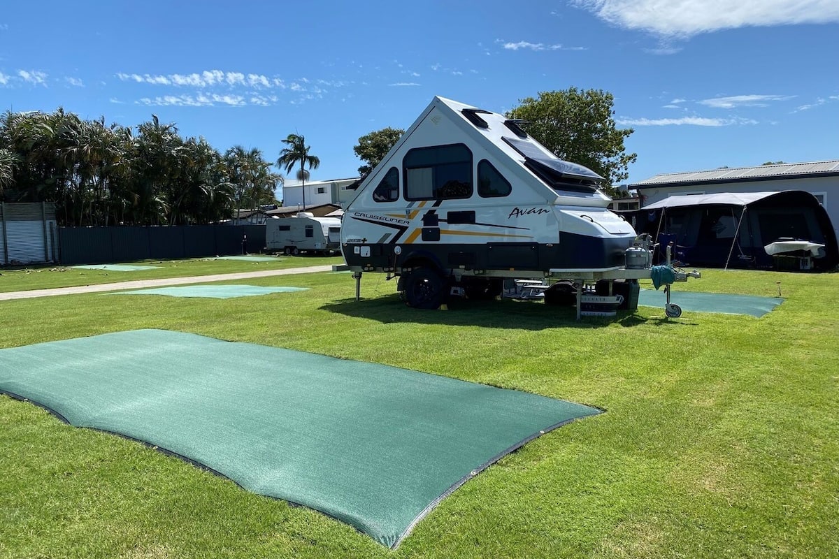 A caravan named 'Avan' parked on a grassy area with a green mat in front.
