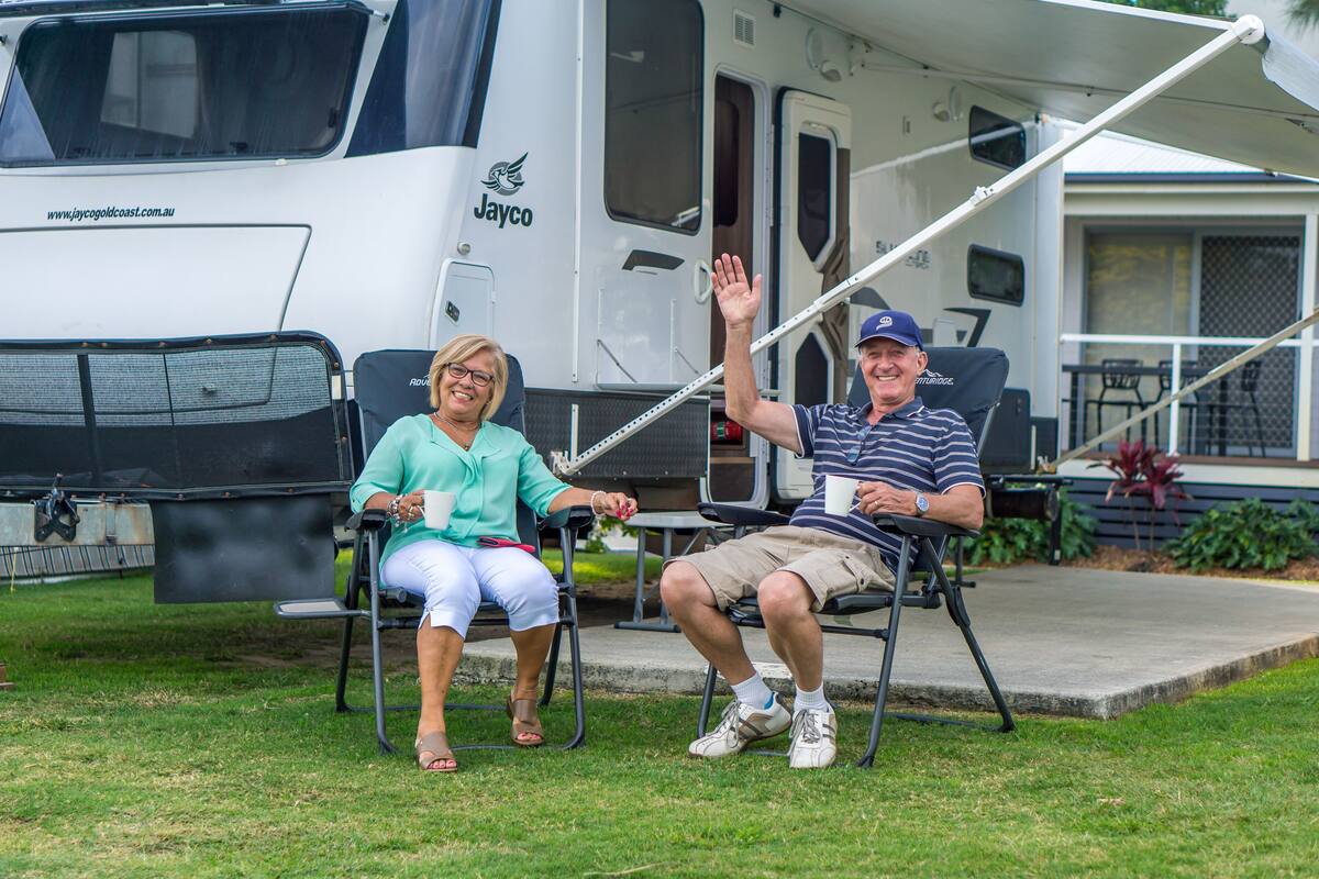 Two people seated on lawn chairs in front of a large RV with a website URL visible on the side.