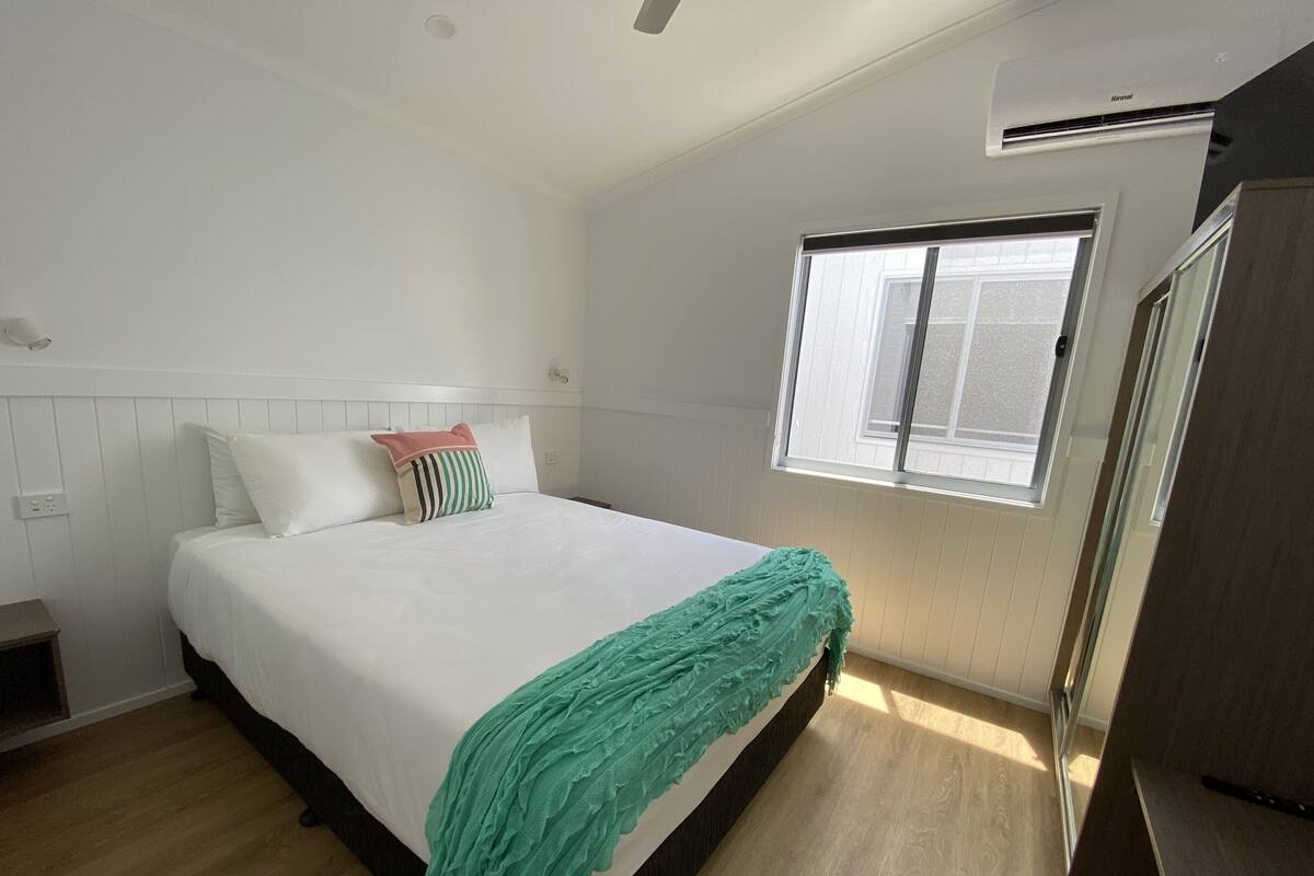 A bedroom with a bed, a window, a wardrobe, and a bedside table.