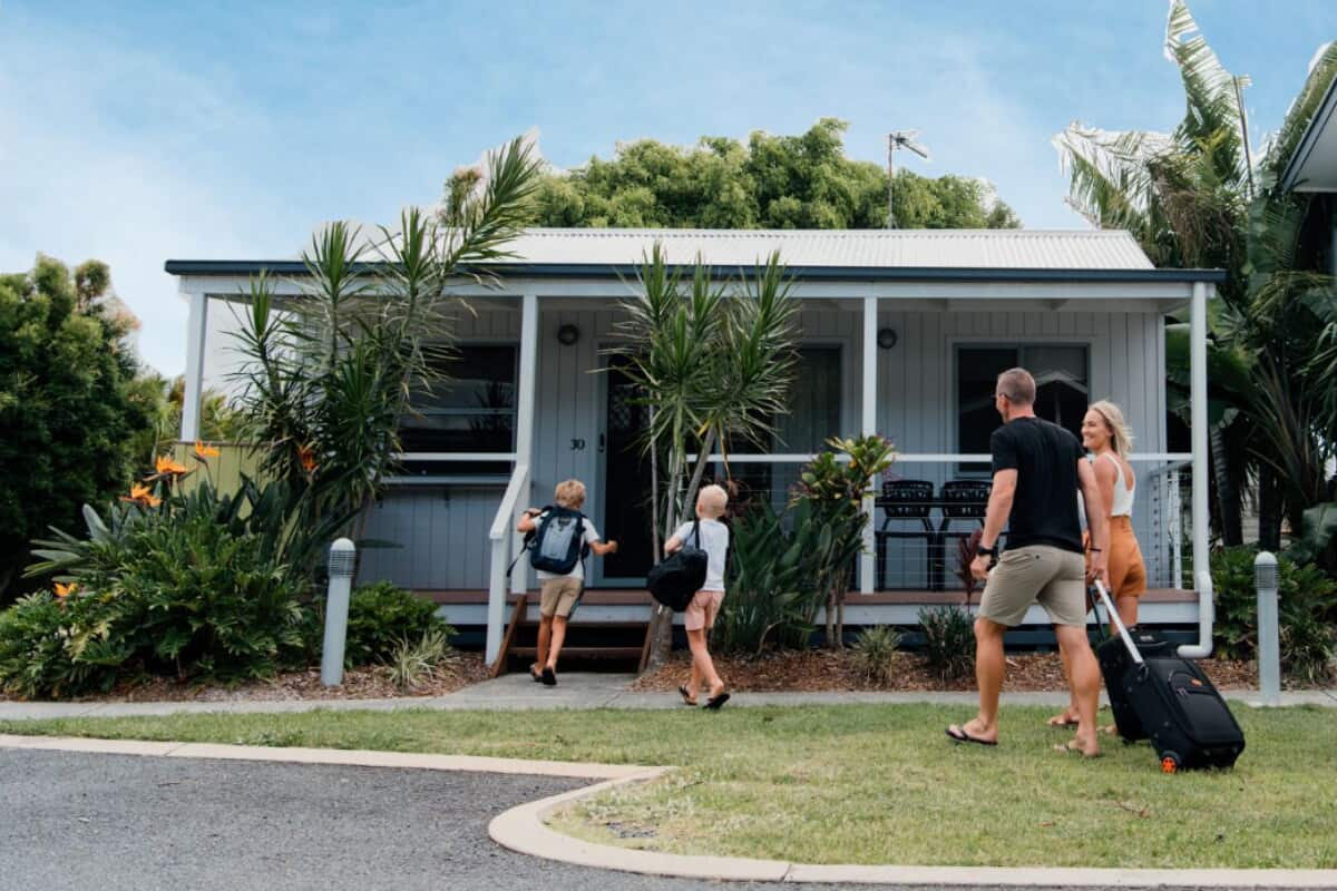 A two-story building with a covered porch and a small garden area with tropical plants.