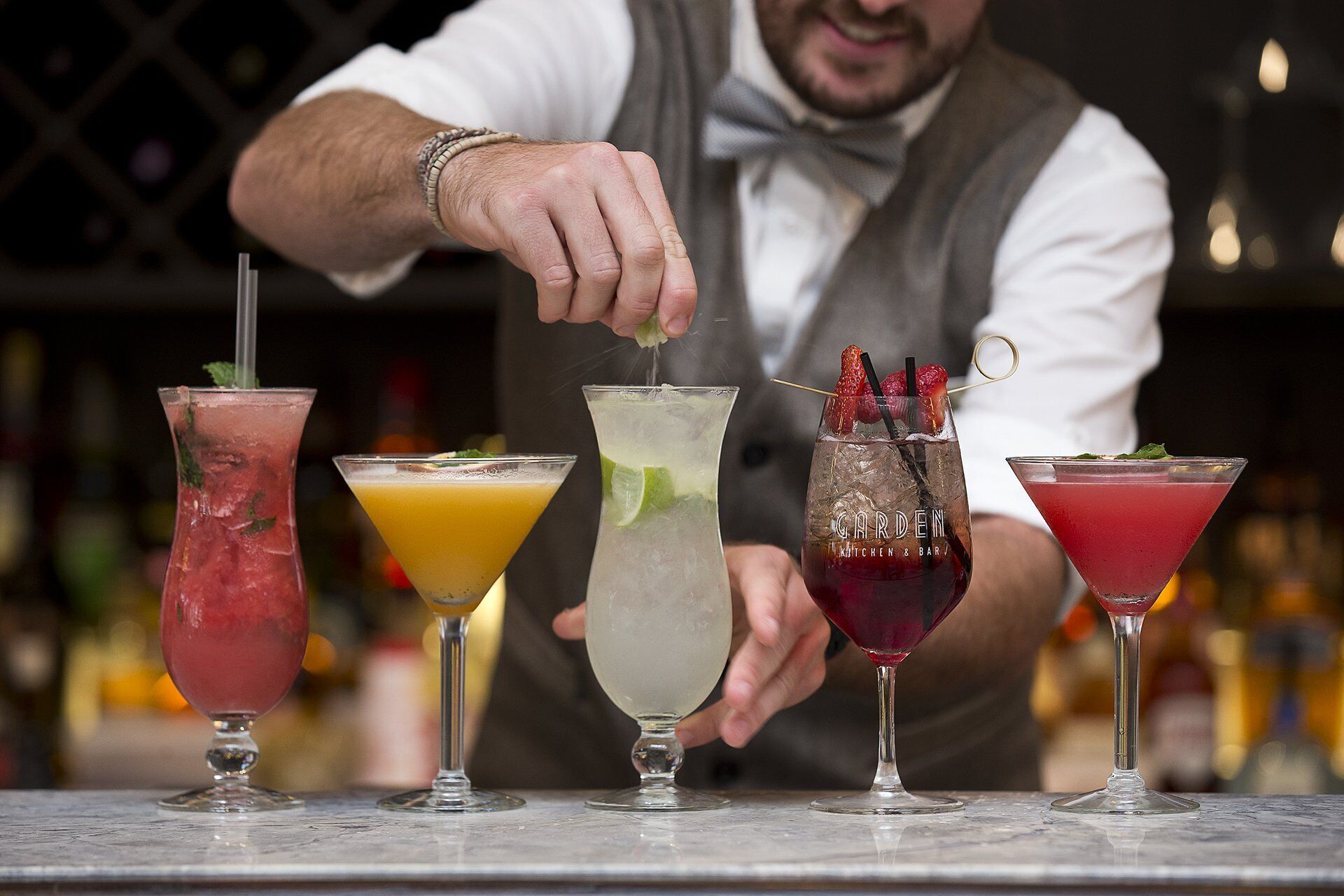 Un barman prépare des cocktails dans différents types de verres au comptoir d’un bar.