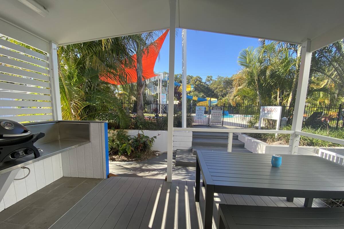 An outdoor patio with a grill, seating area, and a view of a pool and playground.