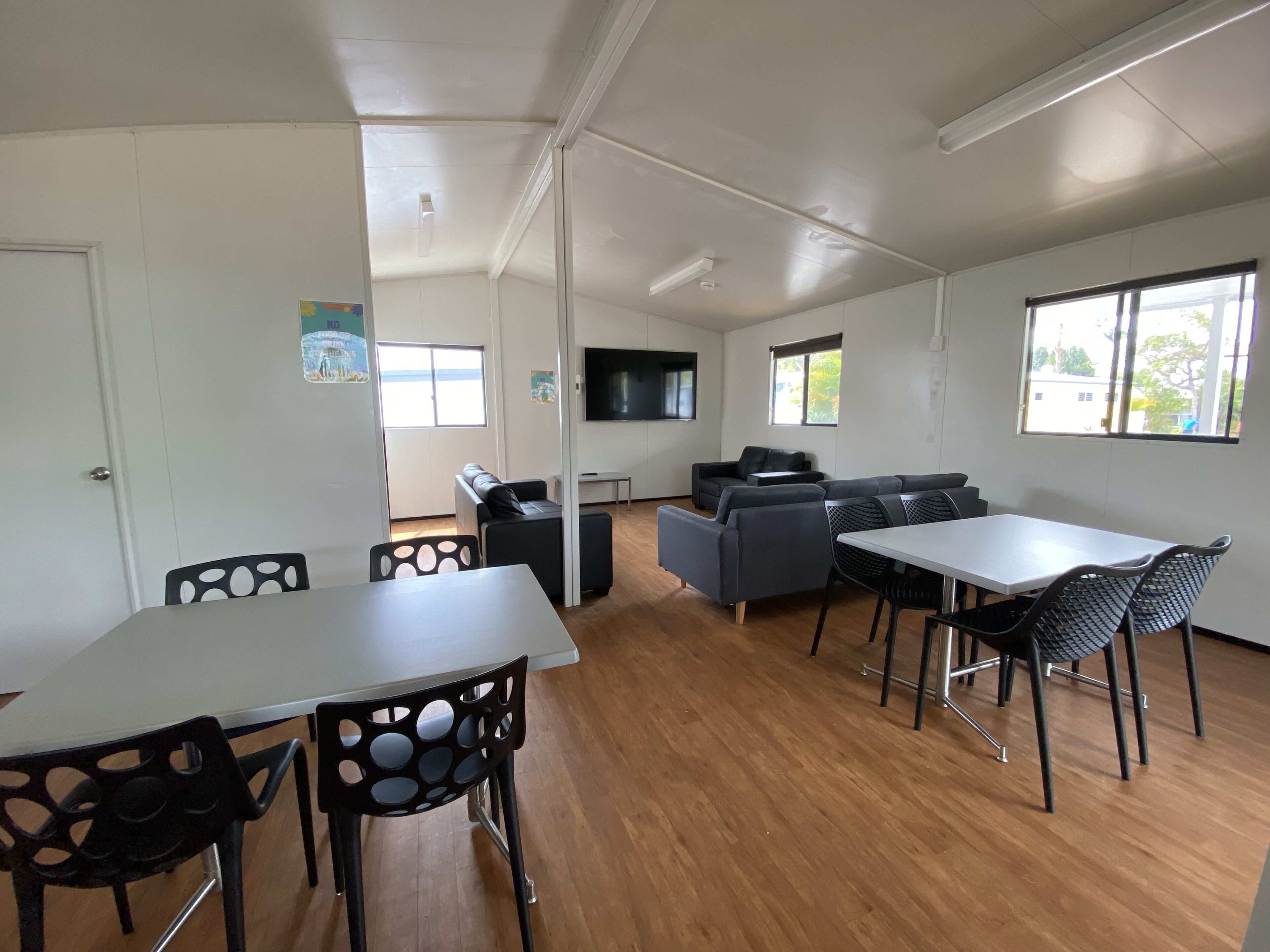 A modern, well-lit room with a dining table, chairs, sofas, and a TV.