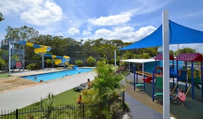 Una piscina con toboganes de agua, una zona de juegos infantiles y un jardín vallado.