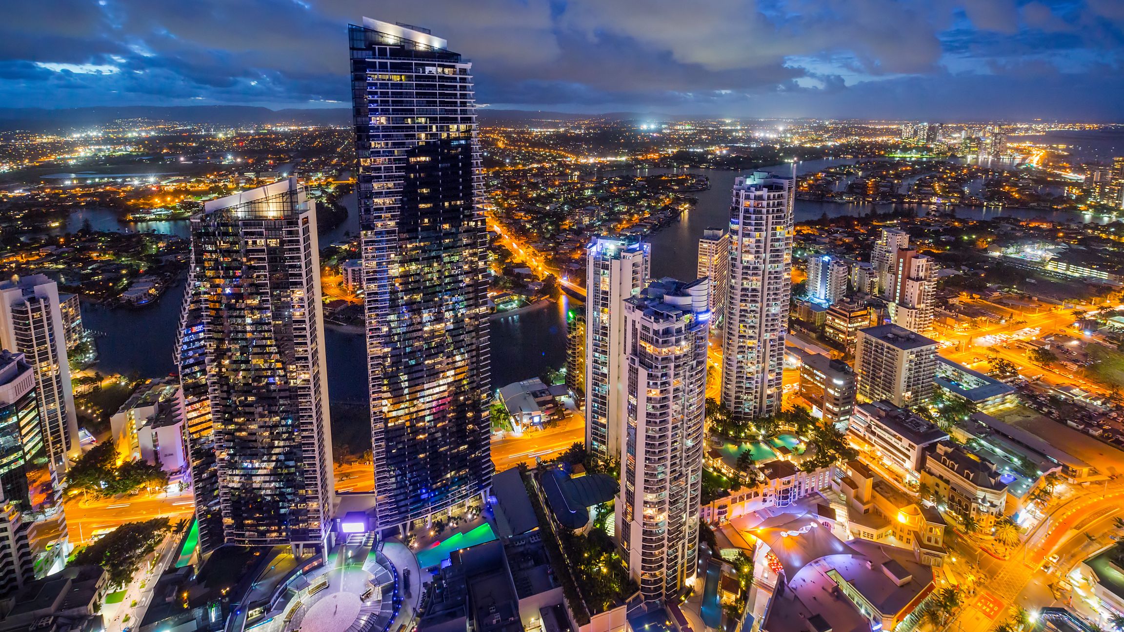 Un complejo de edificios de gran altura con varios rascacielos, un río y una zona urbana iluminada durante la noche.