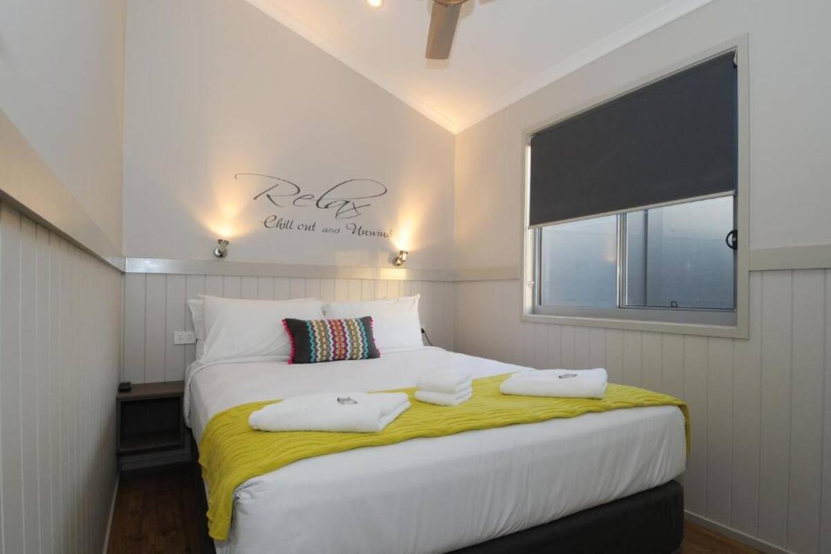 A neatly made bed with white linens, a yellow throw blanket, and a pillow with a multicolored pattern.