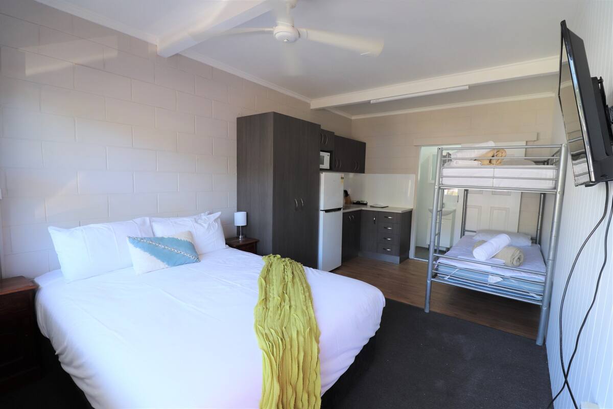 A hotel room with a bed, a small kitchenette, a ceiling fan, and a bunk bed.