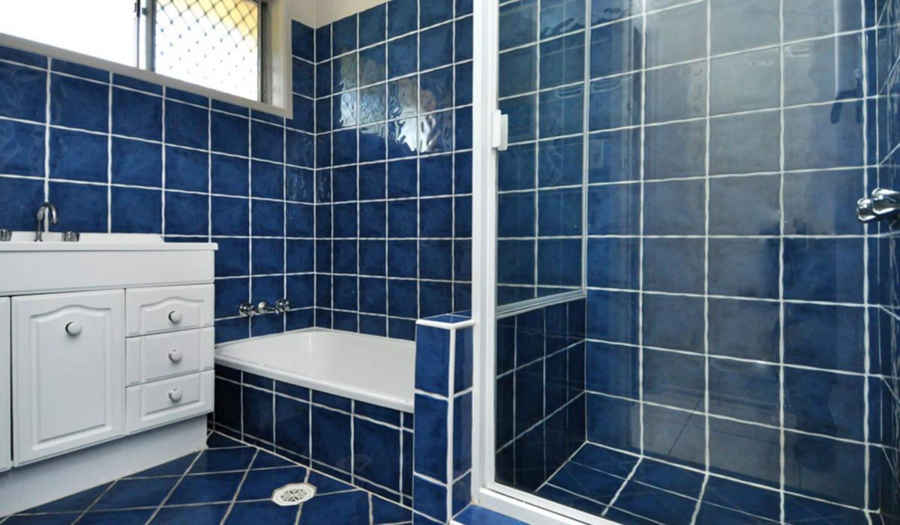 Un baño con azulejos azules, una bañera blanca y un box de ducha.