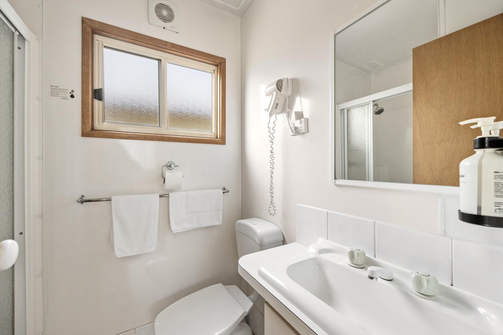 A bathroom with a toilet, sink, and a mirror. There is a towel rack with two towels and a hairdryer on the wall.