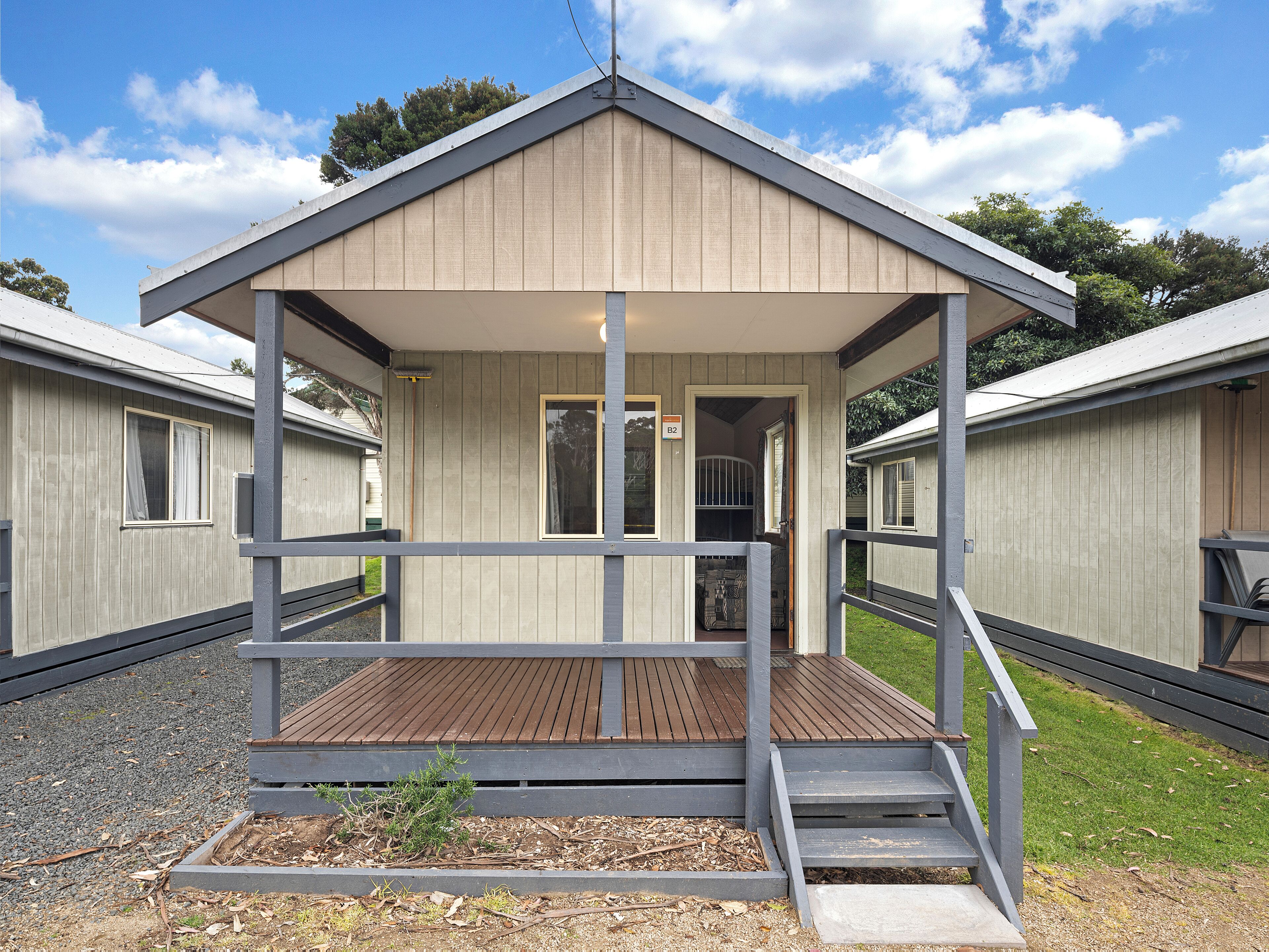 A single-story mobile home with a covered porch, a small front deck, and a gravel driveway.