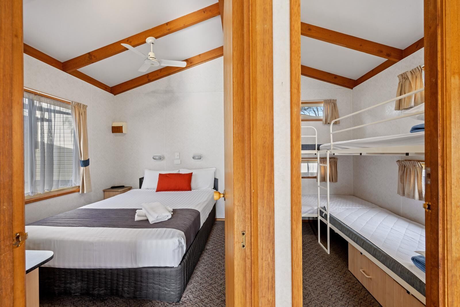 Una habitación con una cama individual, una cama litera, un ventilador de techo y una ventana con cortinas.