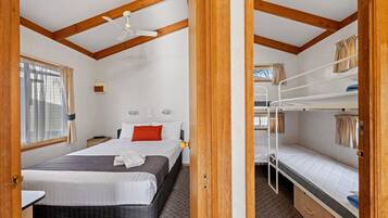 Una habitación con una cama individual, una cama litera, un ventilador de techo y una ventana con cortinas.