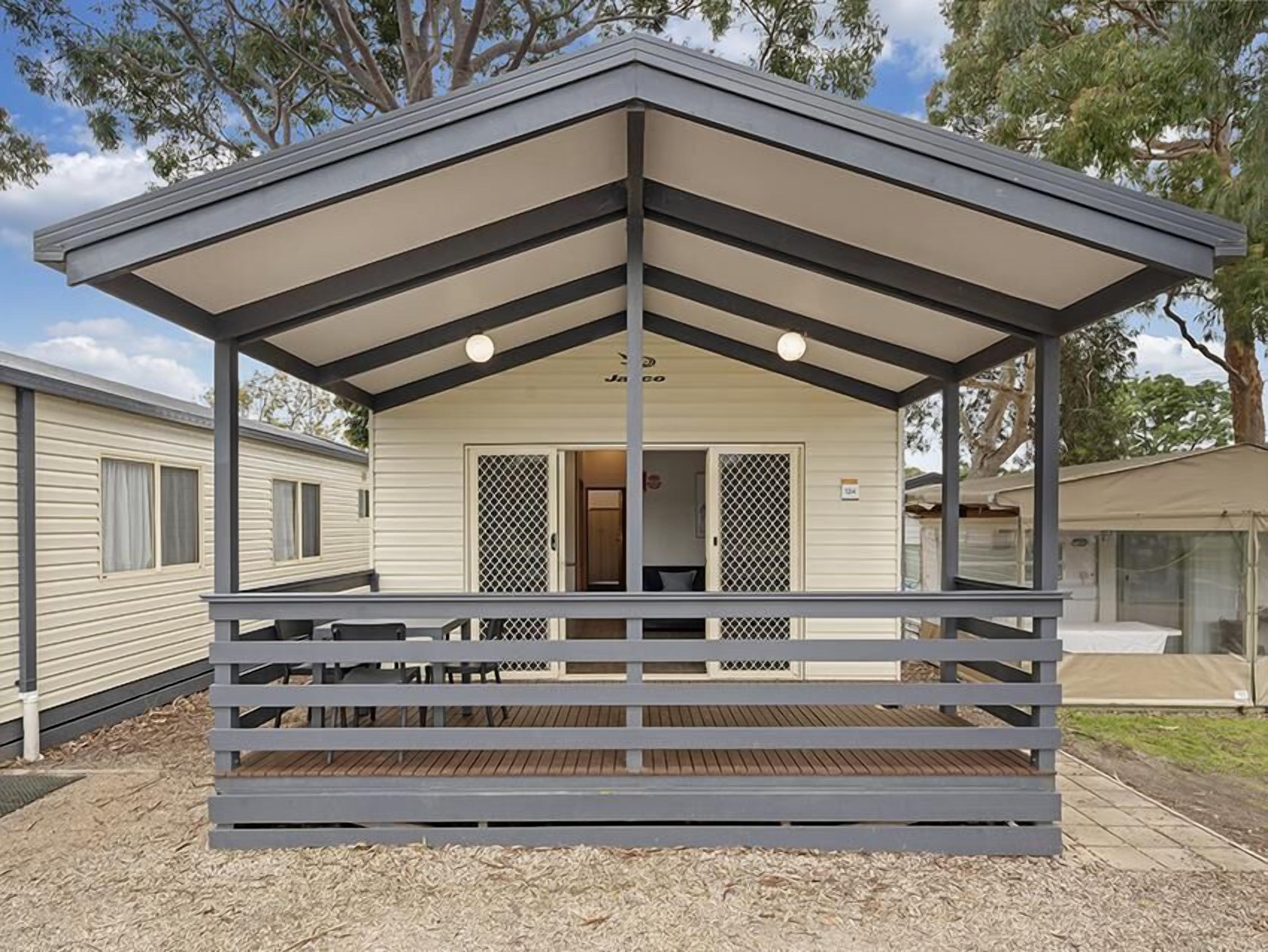A mobile home with a covered porch, a small deck, and a fenced-in area.