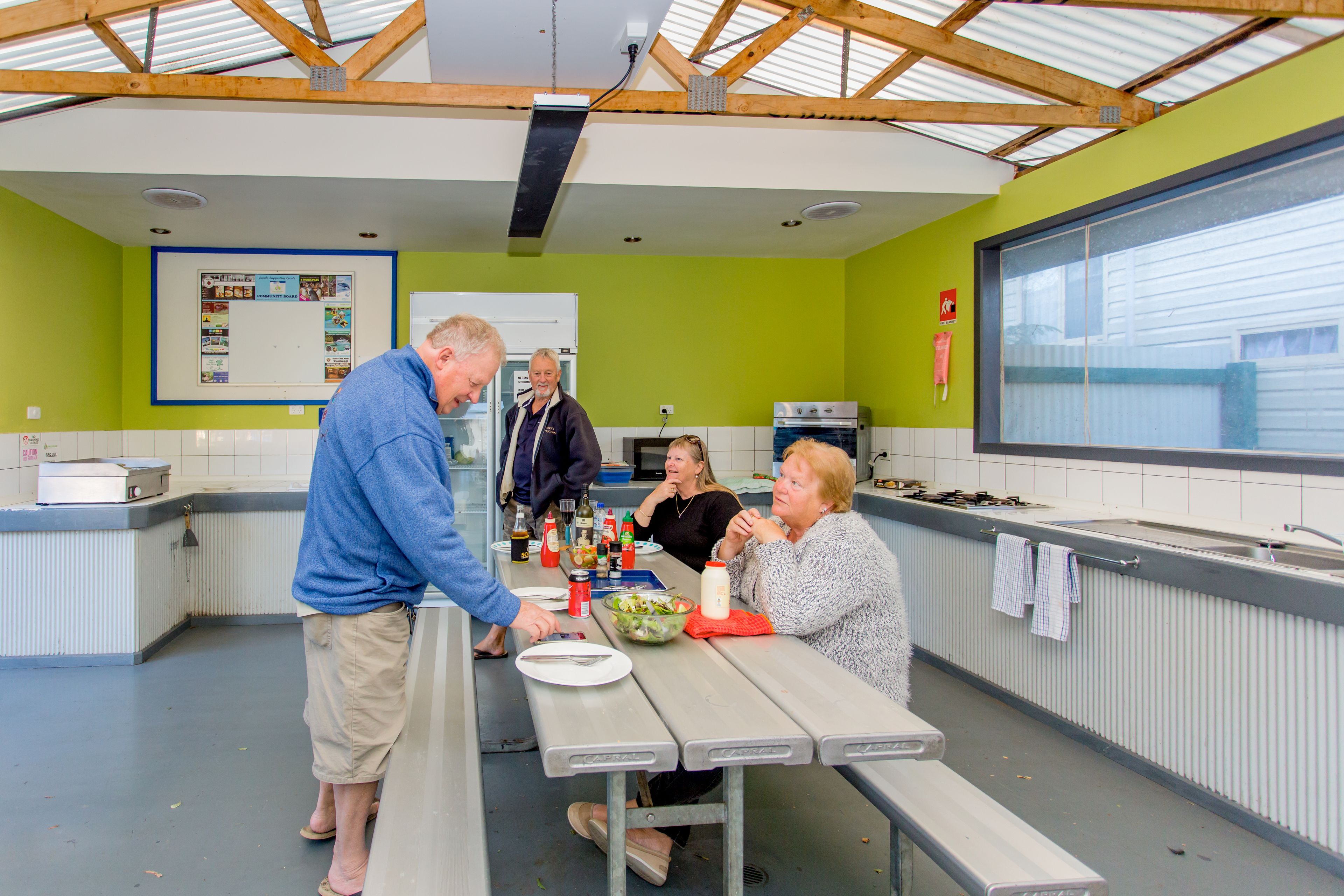 A communal dining area with a long table, a whiteboard, and a kitchen in the background.