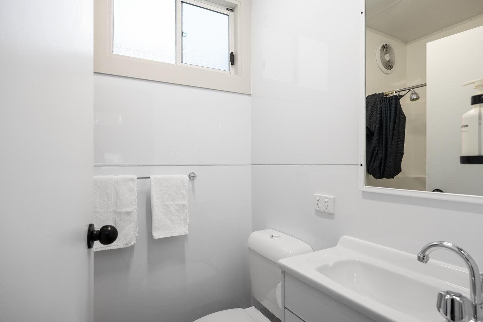 A modern bathroom with a bathtub, a toilet, a towel rack with two white towels, a window, and a mirror.