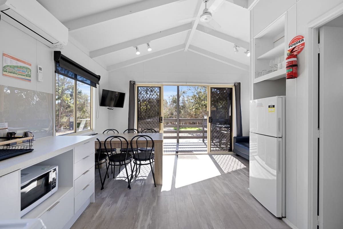 A modern kitchen with a dining area, large windows, and a view of the outdoors.