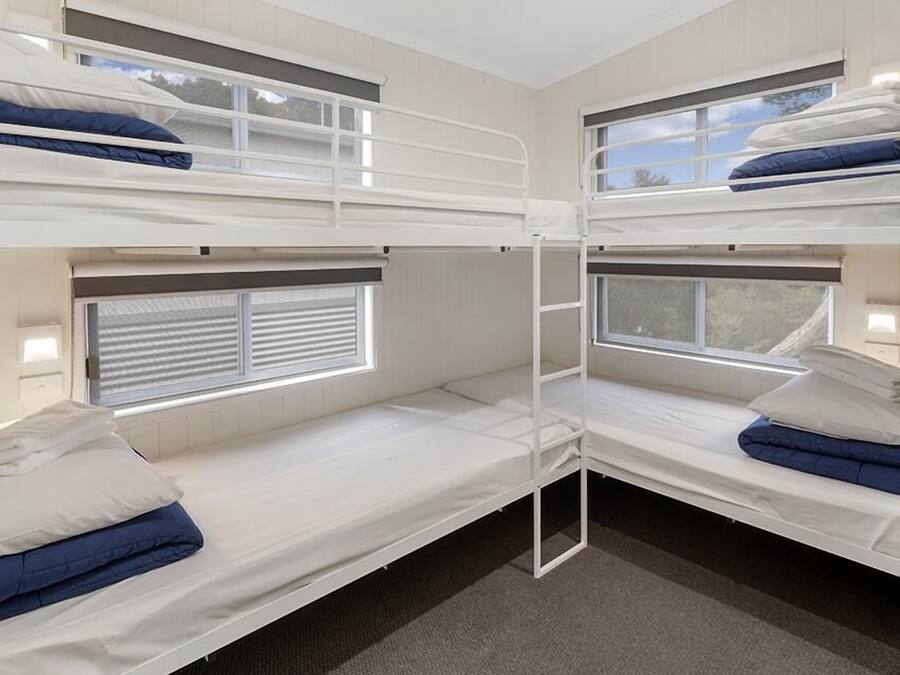 Quarto com beliches, dois leitos cada um com janela e escada.
