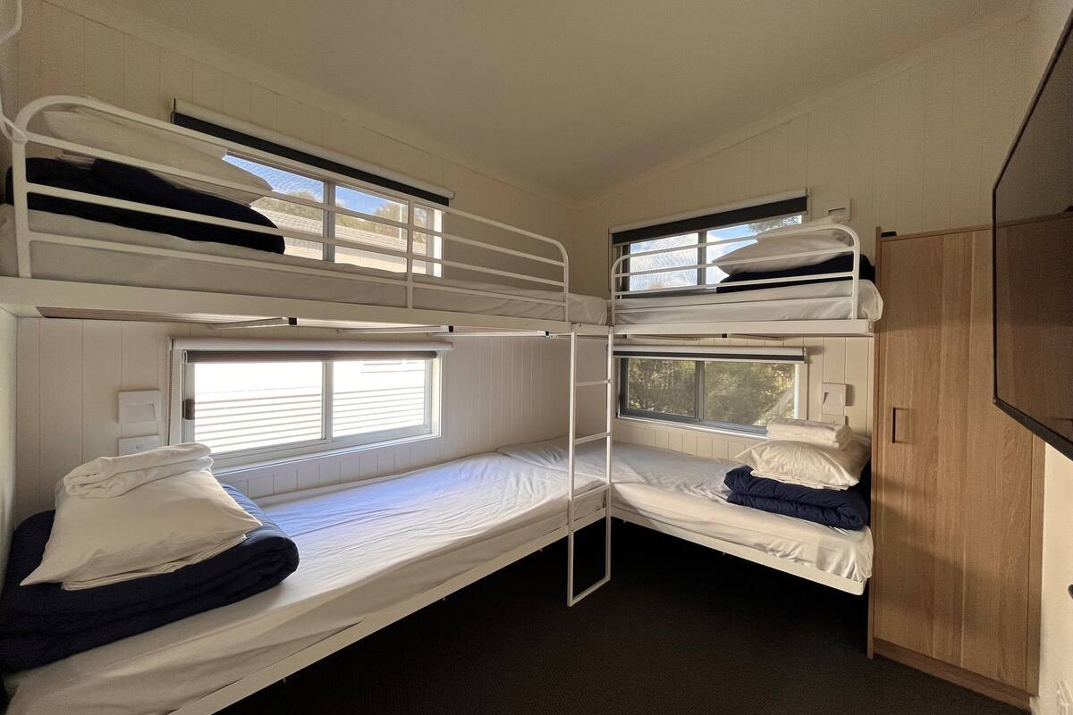 A bunk bed room with a window, a wardrobe, and a small television.