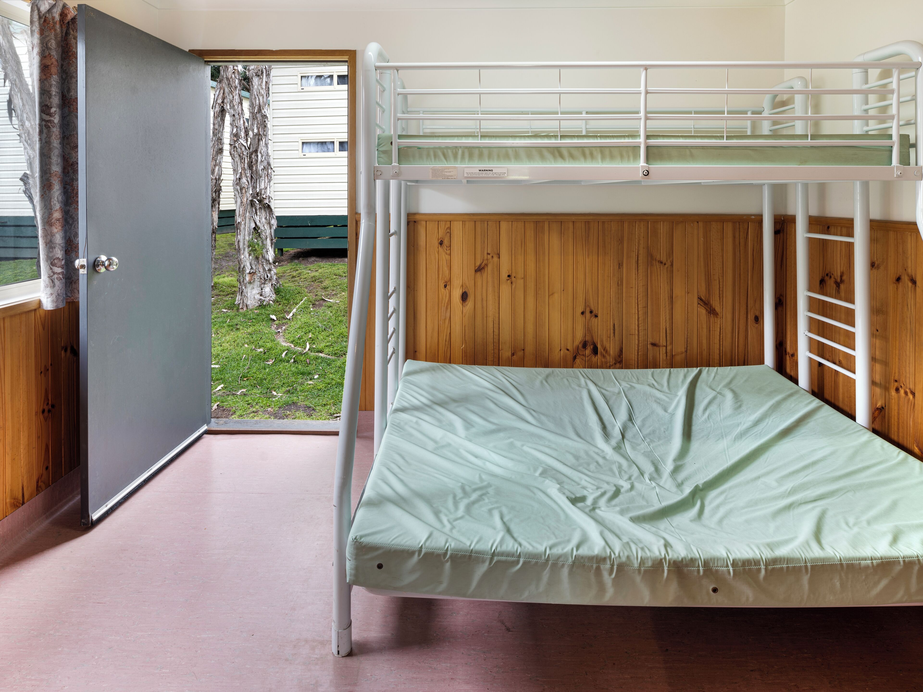 A bunk bed with a green mattress, a wooden panel wall, and a door leading outside.