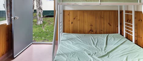 Uma cama beliche com colchão verde, parede de painel de madeira e porta que dá para o exterior.