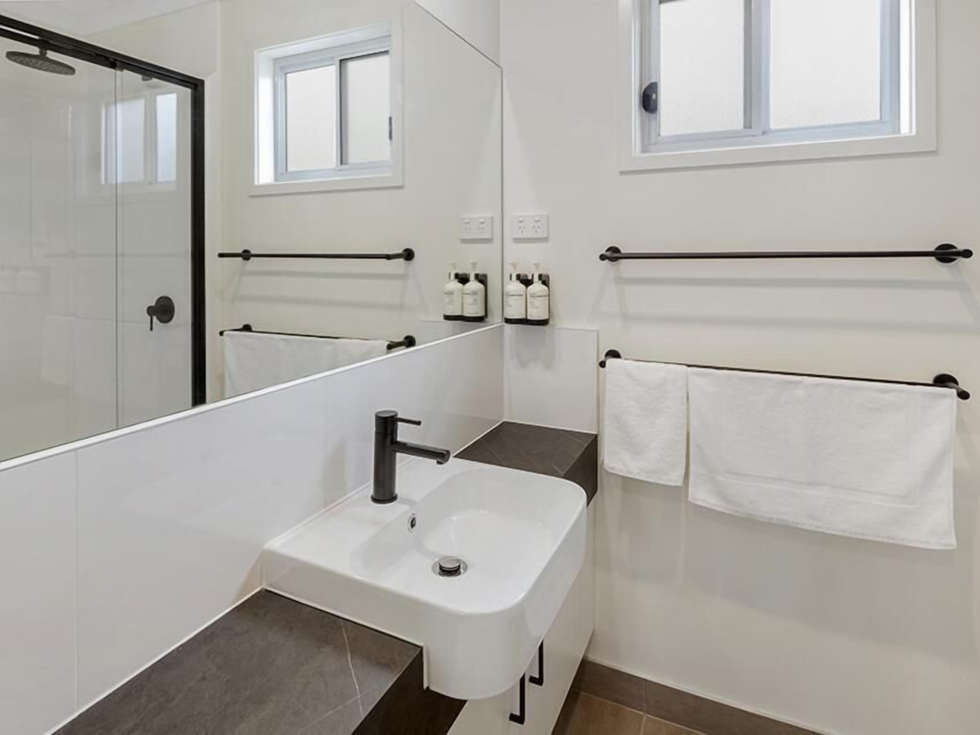 A modern bathroom with a white sink, a mirror, and a towel rack.