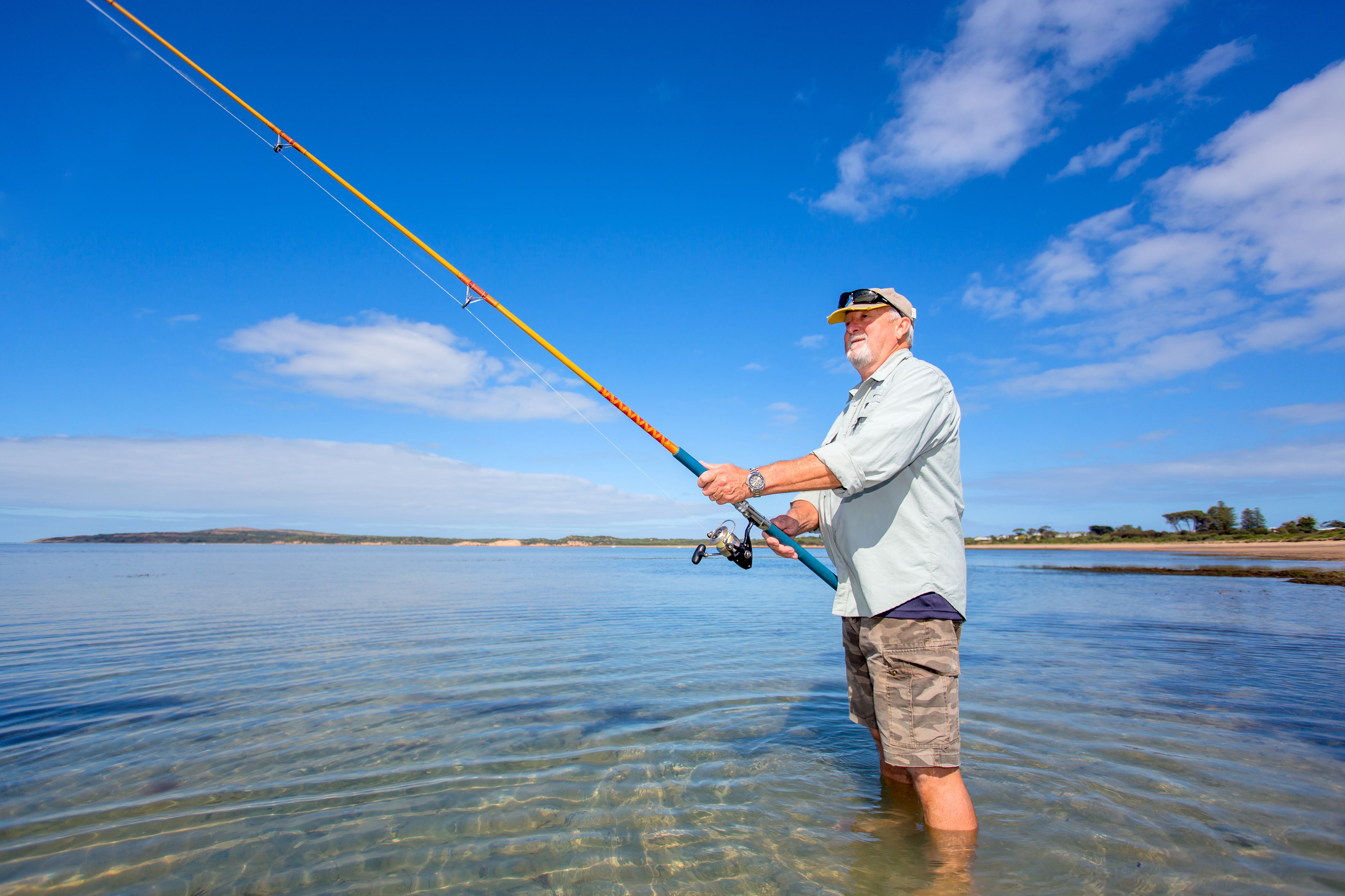 Una persona pescando en aguas poco profundas y transparentes, bajo un cielo despejado.