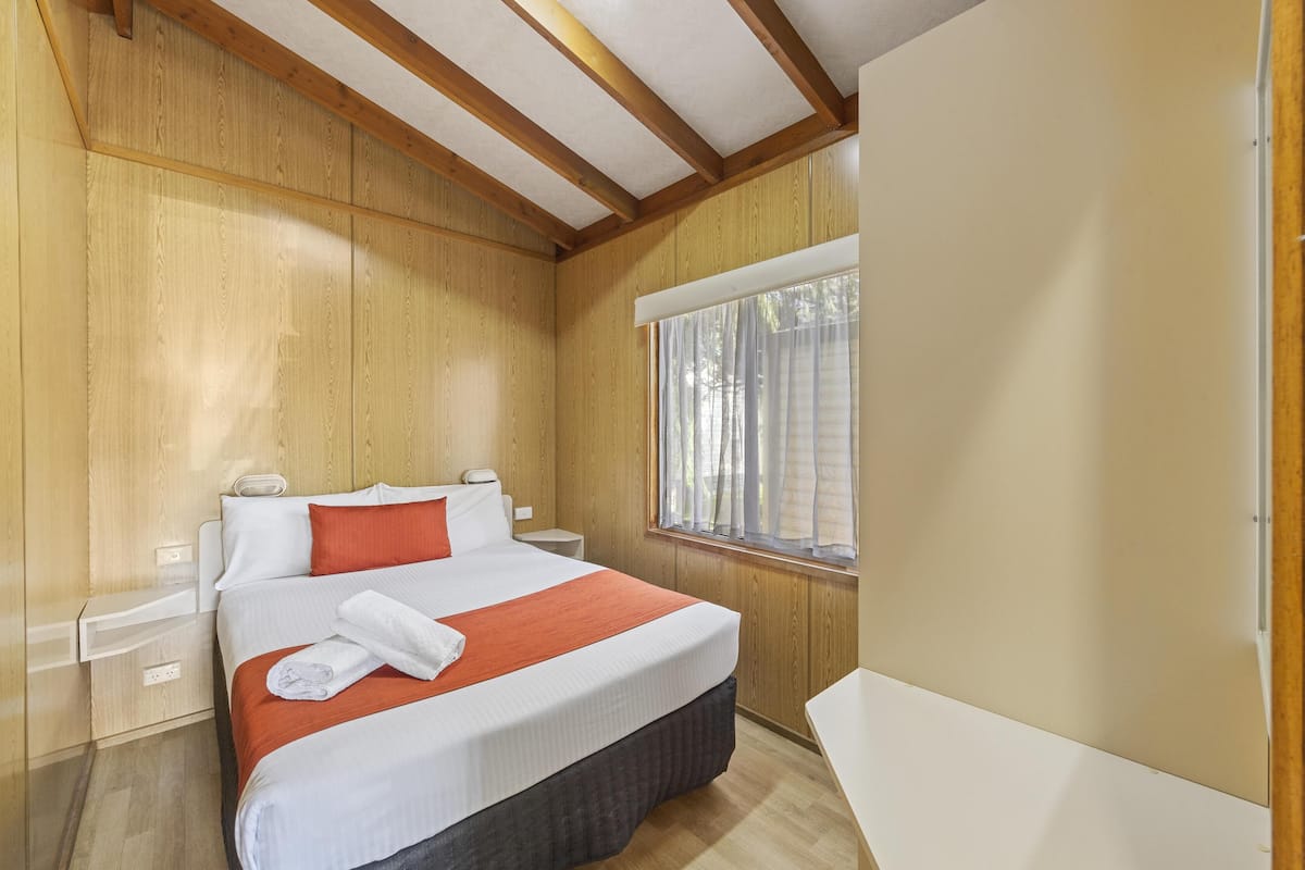 A neatly arranged bedroom with a bed, bedside tables, and a window with curtains.