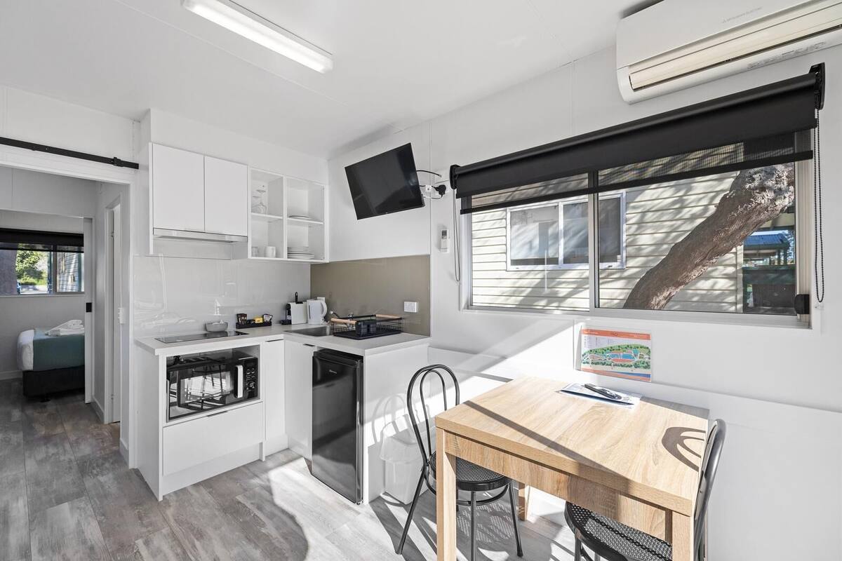 A compact kitchen with white cabinetry, a built-in oven, and a dining area with a wooden table and chairs.