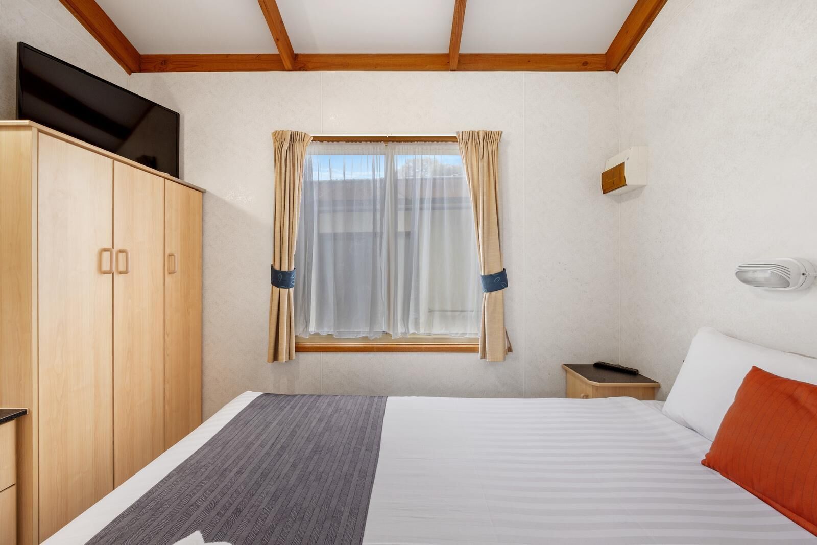 Habitación de hotel con cama, armario, mesita de noche, cortinas y un calentador fijado a la pared.