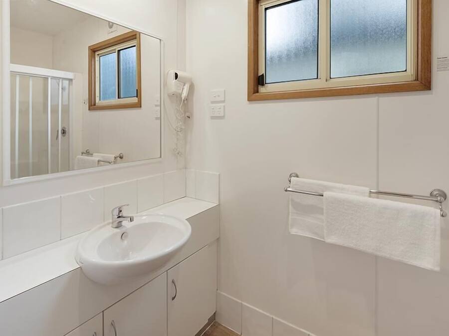 A bathroom with a white sink, a mirror, a towel rack, and a window with frosted glass.