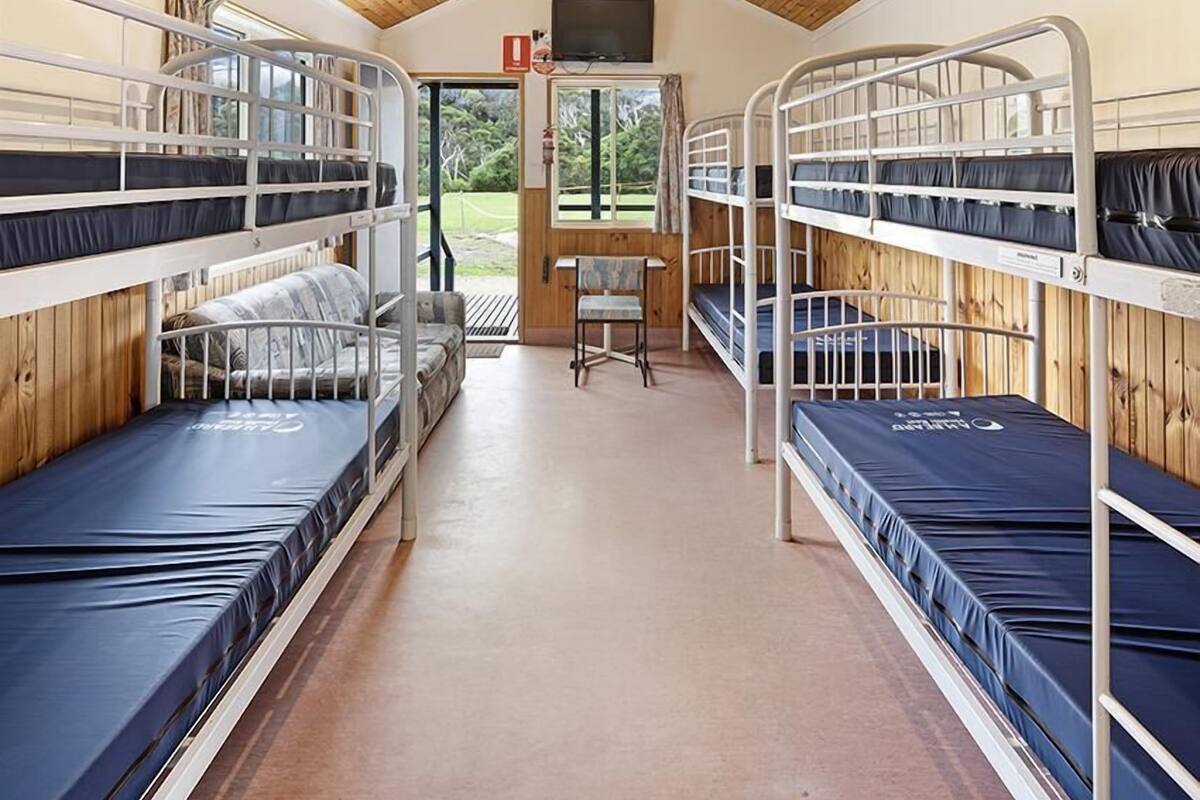 A bunk room with bunk beds, a wooden ceiling, and a door leading outside.
