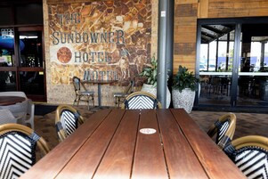 Un área de estar al aire libre con una mesa de madera y sillas de mimbre en The Sundowner Hotel.