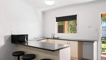 Cocina compacta con encimera negra, microondas integrado, un lavabo y ventana con vista a follaje.