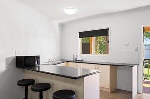 Cocina compacta con encimera negra, microondas integrado, un lavabo y ventana con vista a follaje.