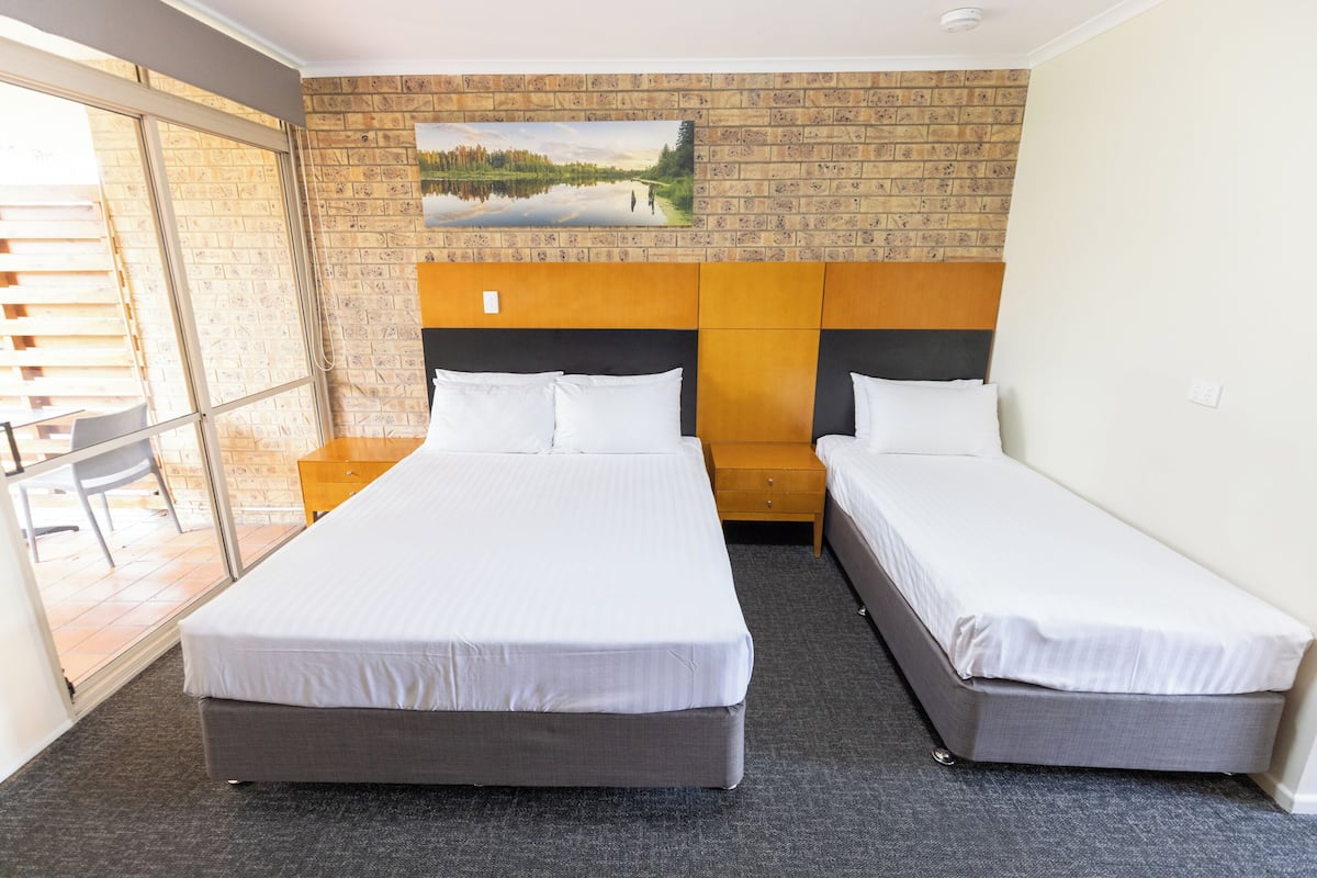 A hotel room with two beds, a brick-patterned wall, and a painting of a lake.