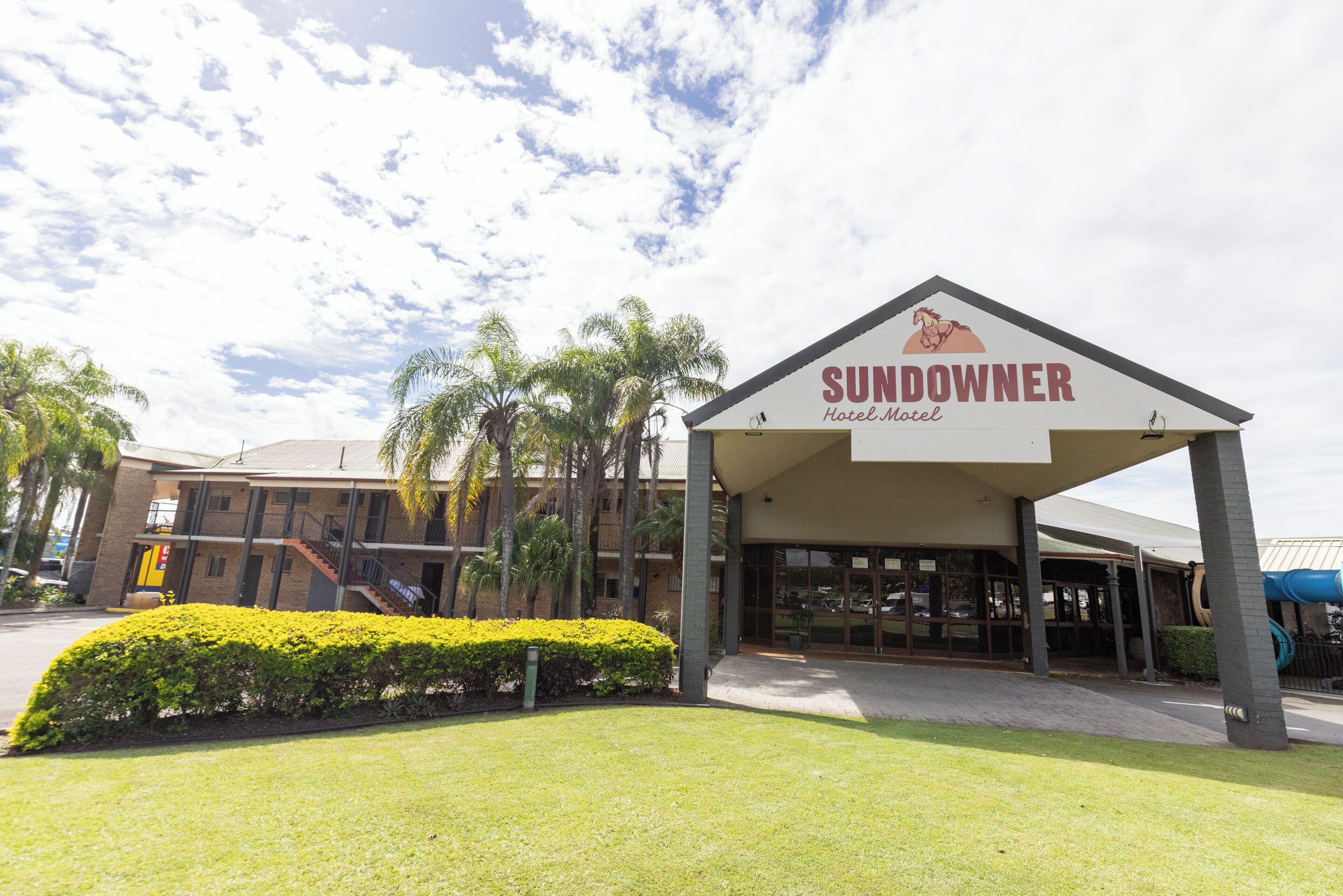 The Sundowner Hotel & Motel with a covered entrance, palm trees, and a clear sky.