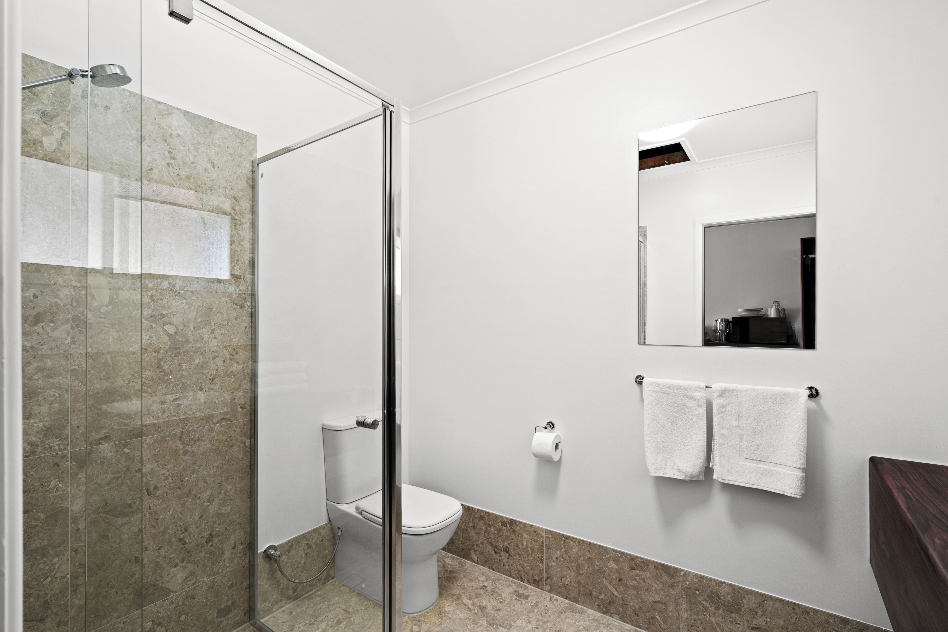 A bathroom with a glass shower enclosure, a toilet, a mirror, and two towels on the wall.